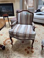Front view of an upholstered bergere chair with striped fabric and wooden frame detailing.