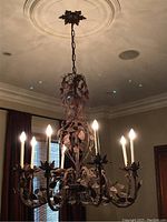 Full view of metal chandelier lit, showing six candlestick-style lights and decorative metal leaves.