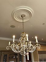 Chandelier hanging from ceiling with multiple candlestick-style lights lit, showing curved scroll arms and chain suspension from decorative ceiling medallion.