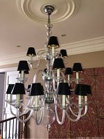 Frontal view of the acrylic chandelier showing black lampshades and clear acrylic arms against a ceiling medallion.