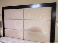 Full view of beige upholstered headboard with six padded panels framed by dark wood base.
