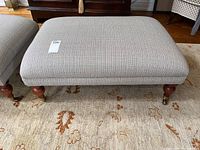 Top-front view of ottoman showing wood legs on casters and fabric upholstery