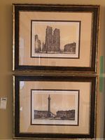 Two framed prints hanging on the wall, top one depicting Notre Dame Cathedral and bottom one showing Place Vendome Column.