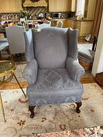 Front view of upholstered wingback chair showing patterned light gray fabric and wooden cabriole legs.