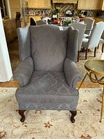 Front view of gray upholstered wingback chair with floral damask pattern and wooden cabriole legs.