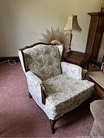 Armchair with floral upholstery, wooden frame, and armrests shown in living room setting.
