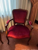 Photo of raspberry velvet upholstered armchair with ornate wooden frame and cabriole legs, showing overall condition and style.