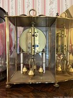 Rear view showing brass frame, pendulum mechanism, and weights inside glass case.