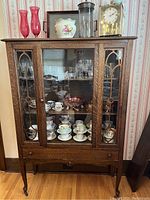 Full frontal view of oak china cabinet with glass doors closed, showcasing wood grain, decorative window muntins, and lower drawer.