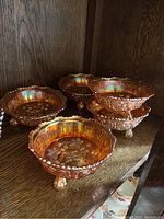 Group view of five smaller footed bowls made of amber-colored carnival glass with embossed butterfly and berry motifs.