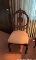 Front view of the wooden side chair showing pink velvet seat and carved circular backrest with floral design