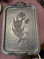 Top view of rectangular hammered metal tray with raised tulip floral design and two ornate handles
