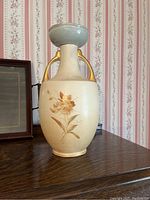 Front view of antique ceramic vase with pale orange floral design and gold handles.