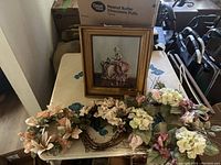 Framed painting of a seated woman in historical attire with floral wreaths and plates on a table