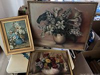 Three framed floral paintings arranged on a surface, showing varying sizes and styles of flower compositions.