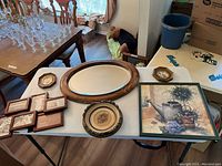 Table with framed art prints, oval mirror, and decorative plates displayed.