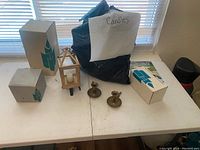 Photo showing boxed candles, brass candle holders, wooden lantern, and other candle accessories arranged on a white table.