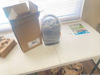 Photo showing a sealed ceramic heater wrapped in plastic standing next to an open box on a table.