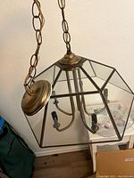 Chandelier showing the brass ceiling mount, chain, and geometric glass frame from a side angle.