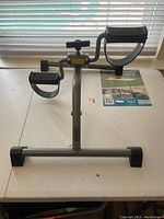Front view of the mini step exercise machine on a white table with pedals and a resistance knob.