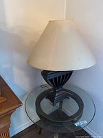 Glass end table supporting the table lamp, showing the clear round glass top and dark base with vertical ribs