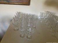 Photo showing multiple clear crystal glasses including wine glasses and cups with stems arranged on a table.