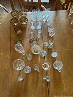 Top view showing assorted glassware including gold floral tumblers, clear wine glasses, shot glasses, and small cups spread on table.