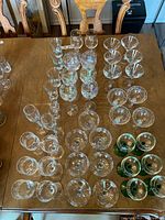 Top down view of multiple wine glasses and cups arranged on a dining table showing clear glass and some with green stems.