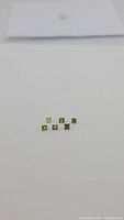 Six small square princess cut apple green peridot gemstones arranged on a white surface.