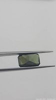 Natural green tourmaline gemstone held by tweezers showing top facet and shape.