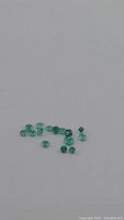 Scattered small bright green diamond-cut Colombian emeralds on a plain background.