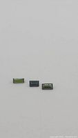 Three baguette cut green tourmaline gemstones displayed together on a light background, showing clarity and color differences.