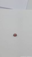 Single oval cut natural spinel gemstone with deep orange color and pink undertone shown on white background, highlighting small surface inclusion.