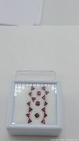 Front view of white gem case with rubies arranged in rows: triangular step-cut rubies flanking central octagonal rubies