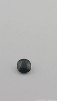Single loose forest green cushion cut sapphire gemstone on a white background, showing top view, highlighting color and faceting.