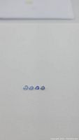 Four natural pear cut blue sapphires arranged in a row on a white background, showing variation in blue shades from light to medium.