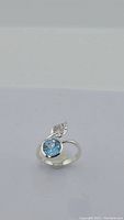 Silver ring with blue round-cut topaz stone and leaf motif photographed on plain background