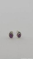 Pair of natural ruby teardrop stud earrings in sterling silver shown side front on white background.
