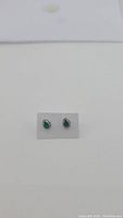 Pair of pear cut vivid green onyx earrings with sterling silver bezel and beaded edges, shown on white card