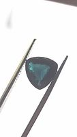 Front view of trillion cut Paraiba blue-green tourmaline held in tweezers showing color and cut