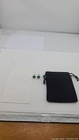 Photo showing pair of green emerald stud earrings with silver settings and black velvet pouch.