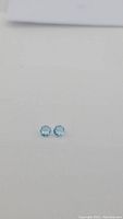 Two small round cut sky blue topaz gemstones placed on a white background, showing size and color.