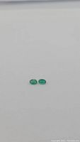 Two small oval cut Zambian emerald gemstones side by side on a plain background, showing size and color.