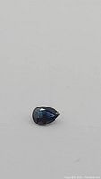 Front view of a pear cut royal blue sapphire gemstone on a white background.
