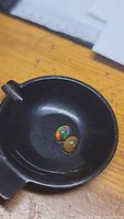 Two oval natural untreated black opal cabochons in a black dish, showing multicolored play of color on one stone and a more opaque brownish body on the other.