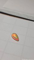 Pear-shaped Ethiopian opal showing vibrant red and green color play on white background grid.