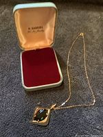 H. Samuel jewelry box and gold chain pendant laid flat on fabric
