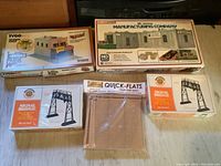 All five model kits arranged on a wooden table, showing boxes for Tyco Barber Shop, Mt. Vernon Manufacturing Company, two Signal Bridge kits, and Quick-Flats building flats.