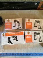 Four sealed Bachmann box kits on a table: Three 'Signal Bridge' kits with illustrated bridge structures, one 'Pedestrian Bridge' kit with photo of black metal pedestrian bridge model.