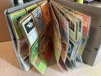 3-ring binder open showing multiple pages of Pokémon cards in sleeves, displaying different Pokémon and energy cards.